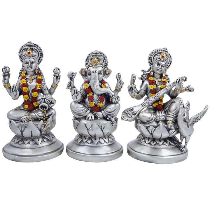 Silver-finish Laxmi Ganesh Saraswati idol set with floral garlands on lotus base for pooja and home decor.